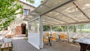 Ein überdachter Patio-Bereich mit Außenbestuhlung, darunter Tische und Stühle sowie eine Bank.