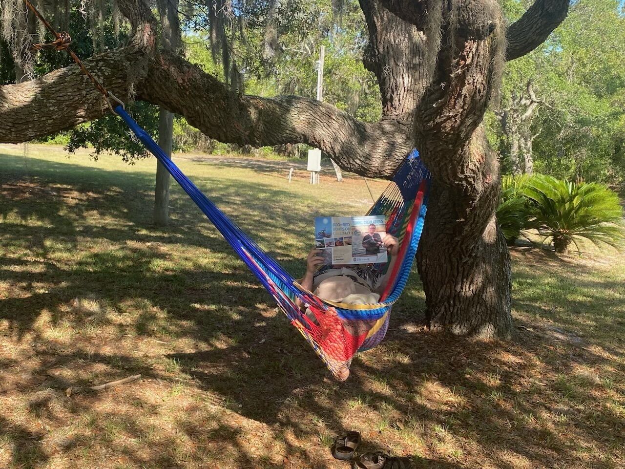 A hammock tied between two trees in a grassy area with a printed newspaper.