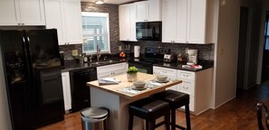 A modern kitchen with white cabinets, a black refrigerator, a microwave, and a coffee maker. - FALL SALE! Pool, Privacy & Family Fun! Mom's Manatee House. (Homosassa)