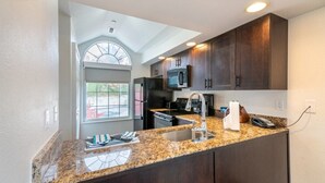 A kitchen with dark wooden cabinets, granite countertops, a built-in microwave, and a large window.