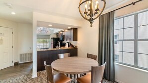 A modern dining area with a round table and chairs, a chandelier, and a view of the kitchen through an open archway.