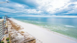 Una playa con vista despejada al océano, un muelle a lo lejos y un hotel con varios pisos y balcones que dan al mar.