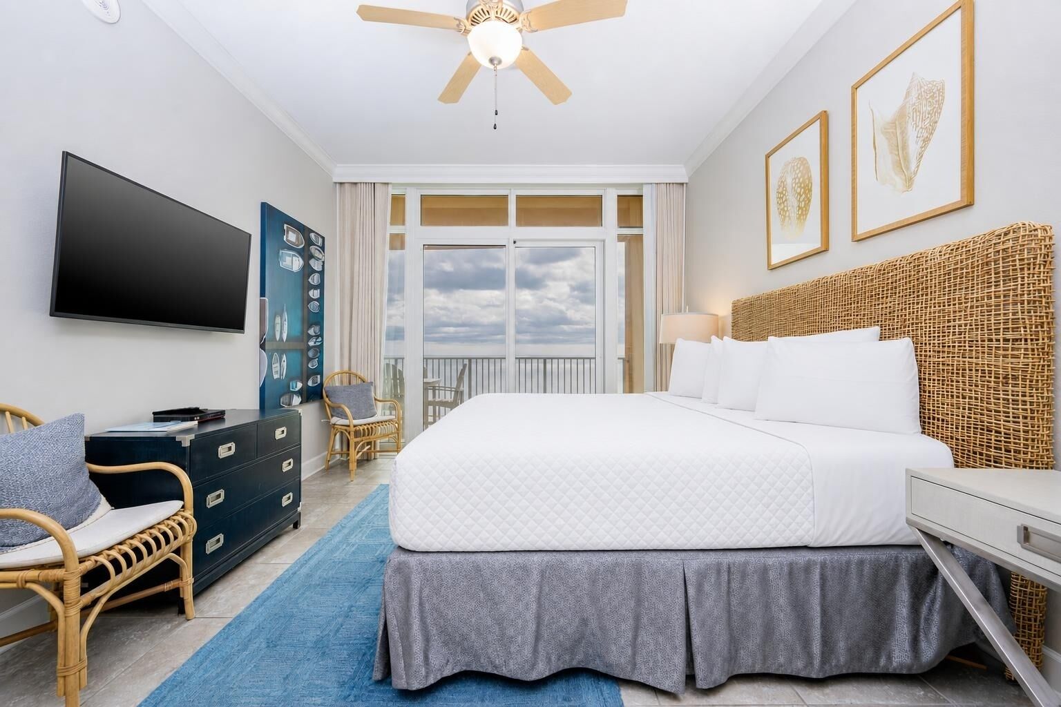 Een hotelkamer met een bed, een televisie, een dressoir, een stoel, een balkon met uitzicht en kunst aan de muur.