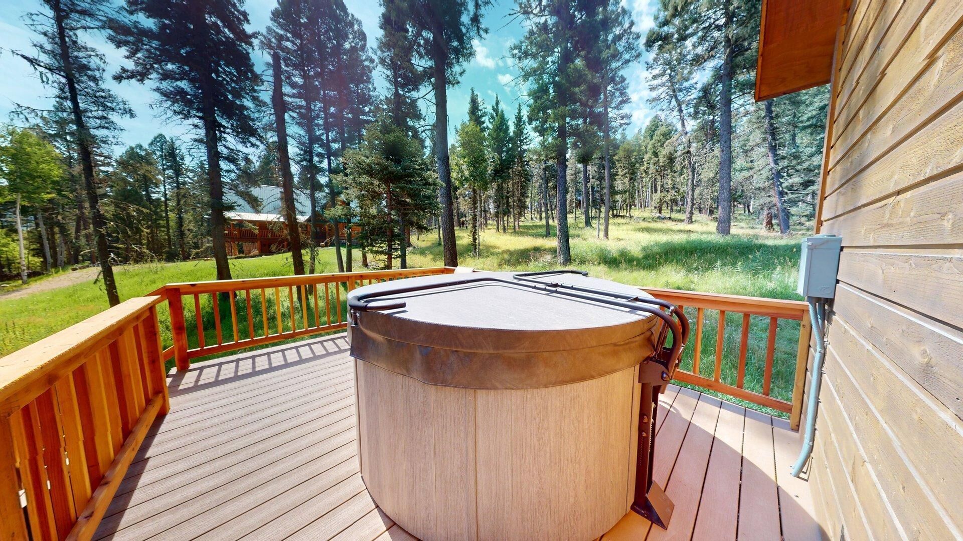A wooden deck with a hot tub, surrounded by a wooden railing, overlooking a forested area.