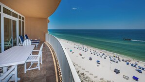 A balcony with a table and chairs overlooking a beach with umbrellas and people.