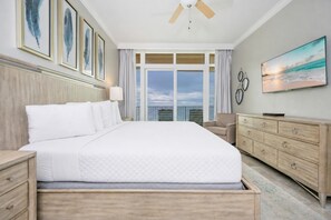 Habitación de hotel con una cama grande, televisión, cómoda y vista al océano.