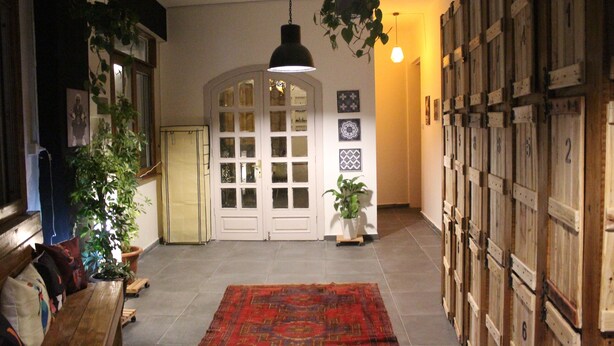 A hallway with a wooden bench, a red patterned rug, a hanging plant, and a row of wooden cabinets with numbers. - The Cabin Hostel (Amman)