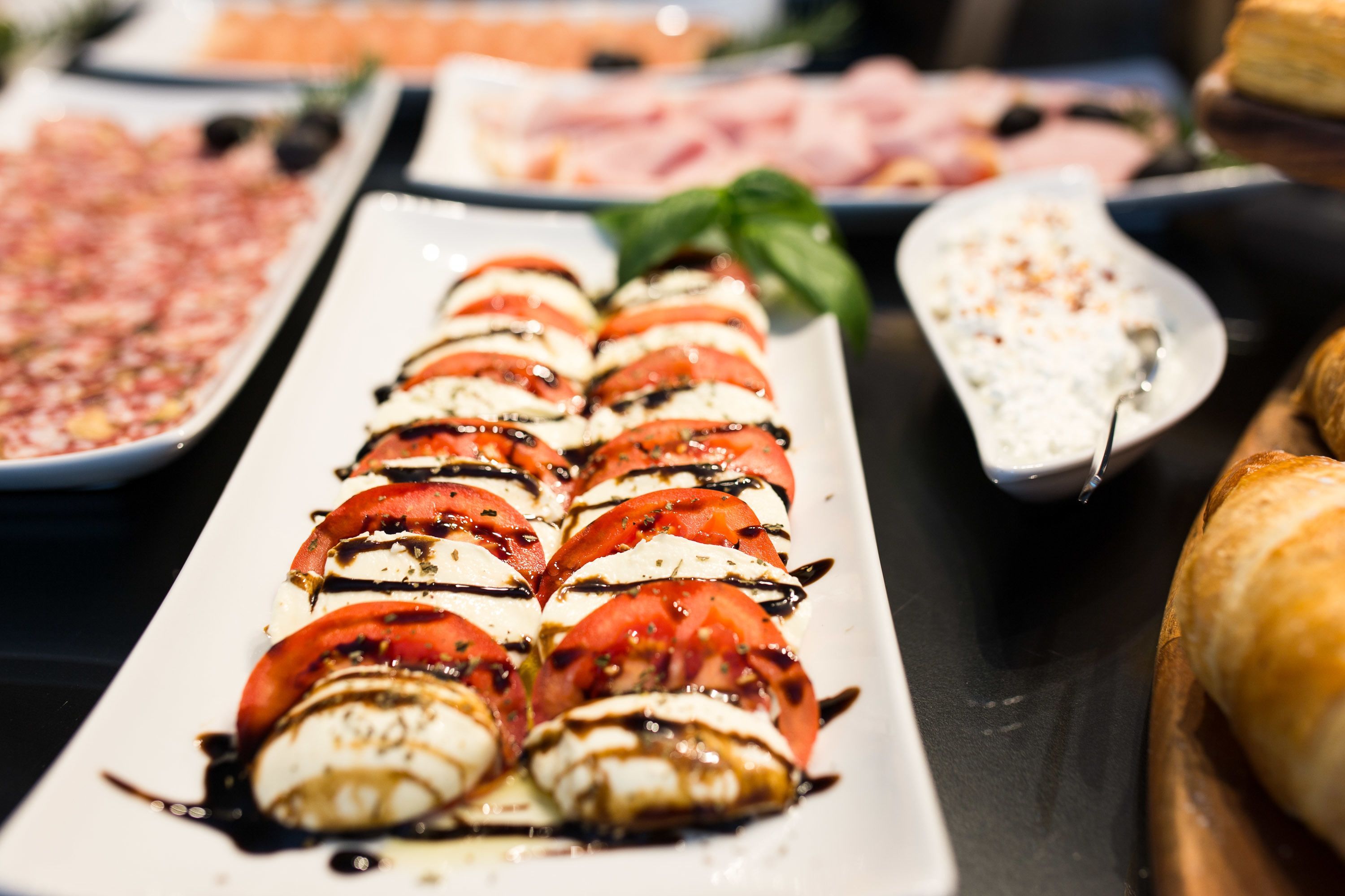 A buffet with various dishes including a plate of caprese salad, a bowl of soup, and a plate of sliced meats.