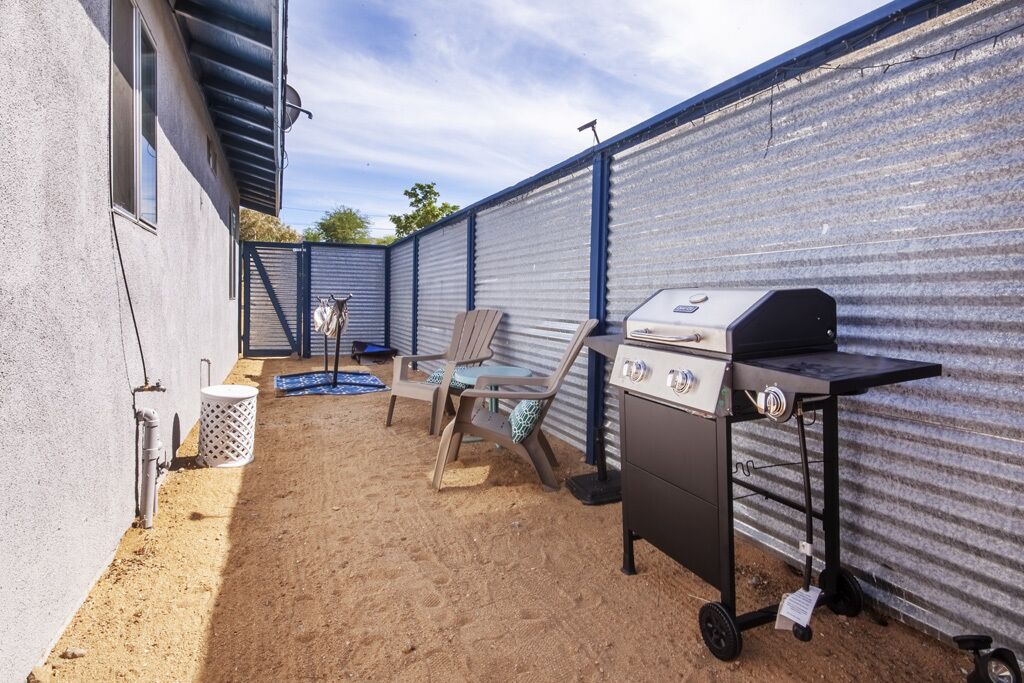 A backyard with a grill, chairs, and a trash can.
