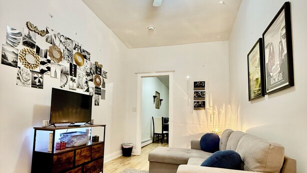Un salon moderne doté d’un ventilateur de plafond, d’un téléviseur à écran plat, d’un meuble en bois, d’un canapé beige et d’un tapis à motifs.