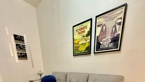 Un canapé d’angle en forme de L avec des coussins bleus, un tapis gris et deux affiches encadrées accrochées au mur.