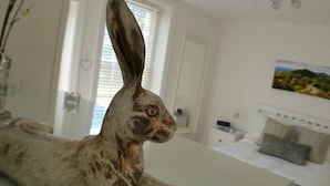 Una escultura de conejo en una habitación moderna de hotel con una cama, una mesita de noche y un cuadro en la pared.
