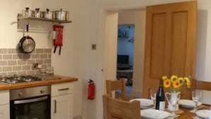 Cocina compacta con estufa, horno y una pequeña zona de comedor con mesa y sillas de madera.