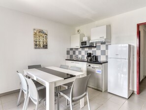 Una cocina compacta con una mesa y sillas, microondas, cafetera y refrigerador.