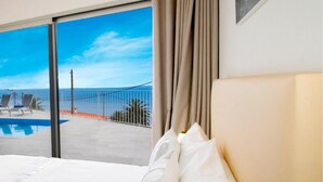 A hotel room with a large bed, a view of a pool and beach, and a painting on the wall. - Beautiful Modern Villa in Calheta – CalhetaScape (Estreito da Calheta)