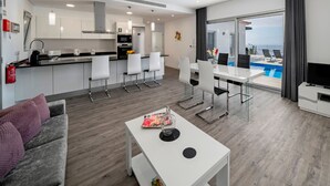 A modern hotel room with a dining area, a kitchen, a living area with a sofa, a TV, and a pool view. - Beautiful Modern Villa in Calheta – CalhetaScape (Estreito da Calheta)