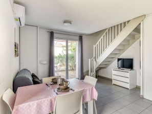 A dining area with a table set for four, a staircase, and a TV in a corner. - Proche du Centre-ville! + Accès piscine extérieure (ARGELES-SUR-MER)