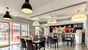 Un restaurante moderno con barra, varias mesas y sillas, y amplios ventanales que ofrecen vistas al exterior.