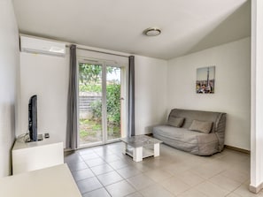 A living room with a sofa, a coffee table, a TV, and a sliding glass door leading to a garden. - Maison à 5 minutes de la Plage, avec accès piscine (ARGELES-SUR-MER)