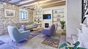 Ein gemütliches Wohnzimmer mit Steinwand, Holzbalken, Kamin und Fernseher.
