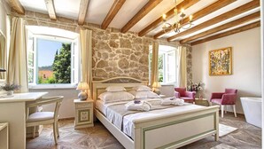 Ein Schlafzimmer mit Steingemäuer, einem Bett mit weißen Leinen, einem Schreibtisch mit Stuhl und einer Kristallleuchter.