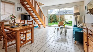 Amplia sala de estar con una escalera de madera, una mesa de comedor con sillas, un sofá y un televisor.