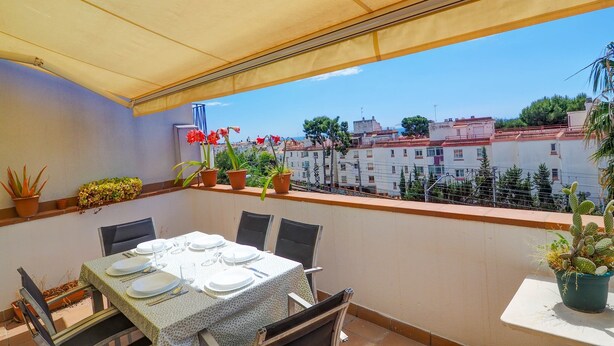 Varanda com mesa posta para refeições, plantas em vasos e vista para edifícios.