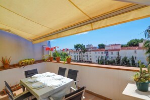 A balcony with a table set for dining, potted plants, and a view of buildings.