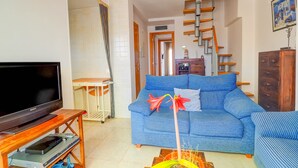 Sala de estar com sofá azul, móvel de madeira para TV, escada e um quadro na parede.