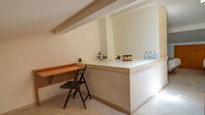 Quarto pequeno e bem iluminado, com escrivaninha, cadeira, cama e guarda-roupa de madeira.