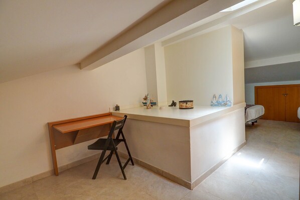 A small, well-lit room with a desk and chair, a bed, and a wooden wardrobe.