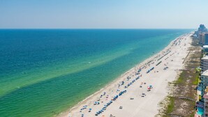 Ein Strand mit Reihen von Sonnenschirmen und Liegestühlen, ein klares blaues Meer und Gebäude entlang der Küste.