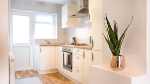 A compact kitchen with white cabinets, a stainless steel oven, a sink, and a potted plant. - Generous Home near Liberty Stadium (Swansea)
