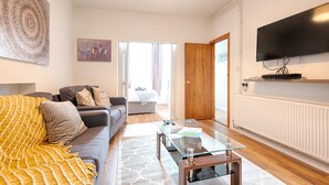 A modern living room with a sofa, coffee table, and a flat-screen TV mounted on the wall. - Generous Home near Liberty Stadium (Swansea)