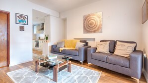 A modern living room with two grey sofas, a glass coffee table, and a patterned rug. - Generous Home near Liberty Stadium (Swansea)