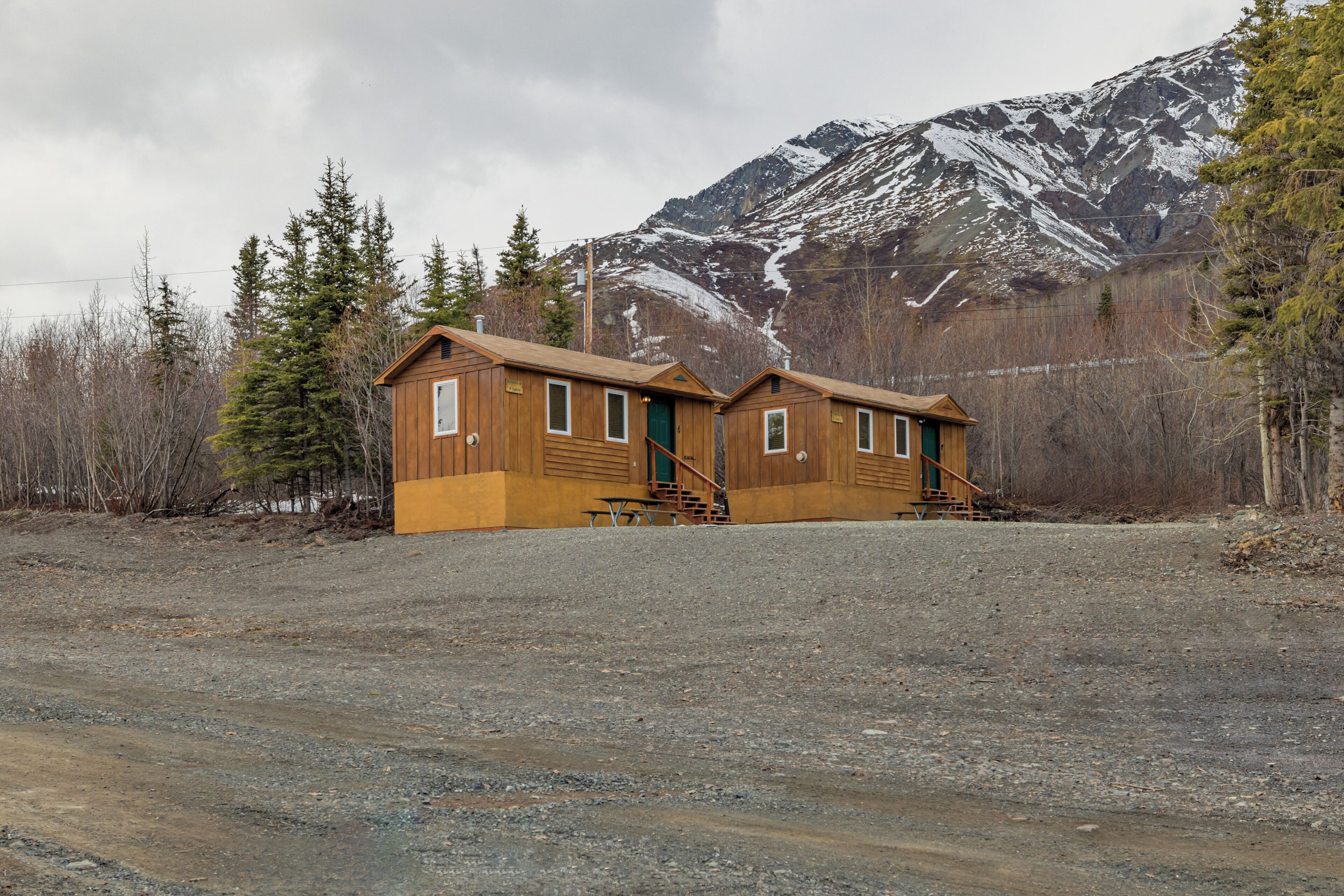 A two-story wooden cabin with a front porch, a staircase, and a view of a snow-capped mountain.