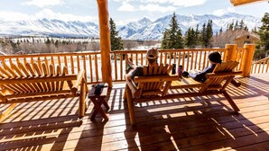 A wooden deck with two wooden chairs and a small table, overlooking a snowy mountain range. - Majestic Valley Wilderness Lodge (Sutton)