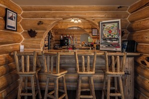 A log cabin interior with a bar area featuring wooden stools, a coffee machine, and a large decorative pinball machine. - Majestic Valley Wilderness Lodge (Sutton)