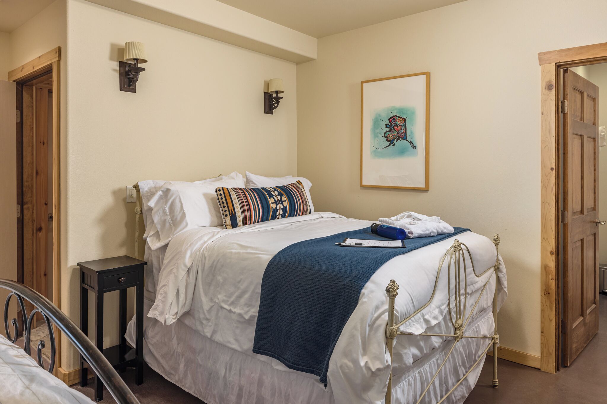 Un dormitorio con cama, mesita de noche, lámpara, obra de arte y una puerta.