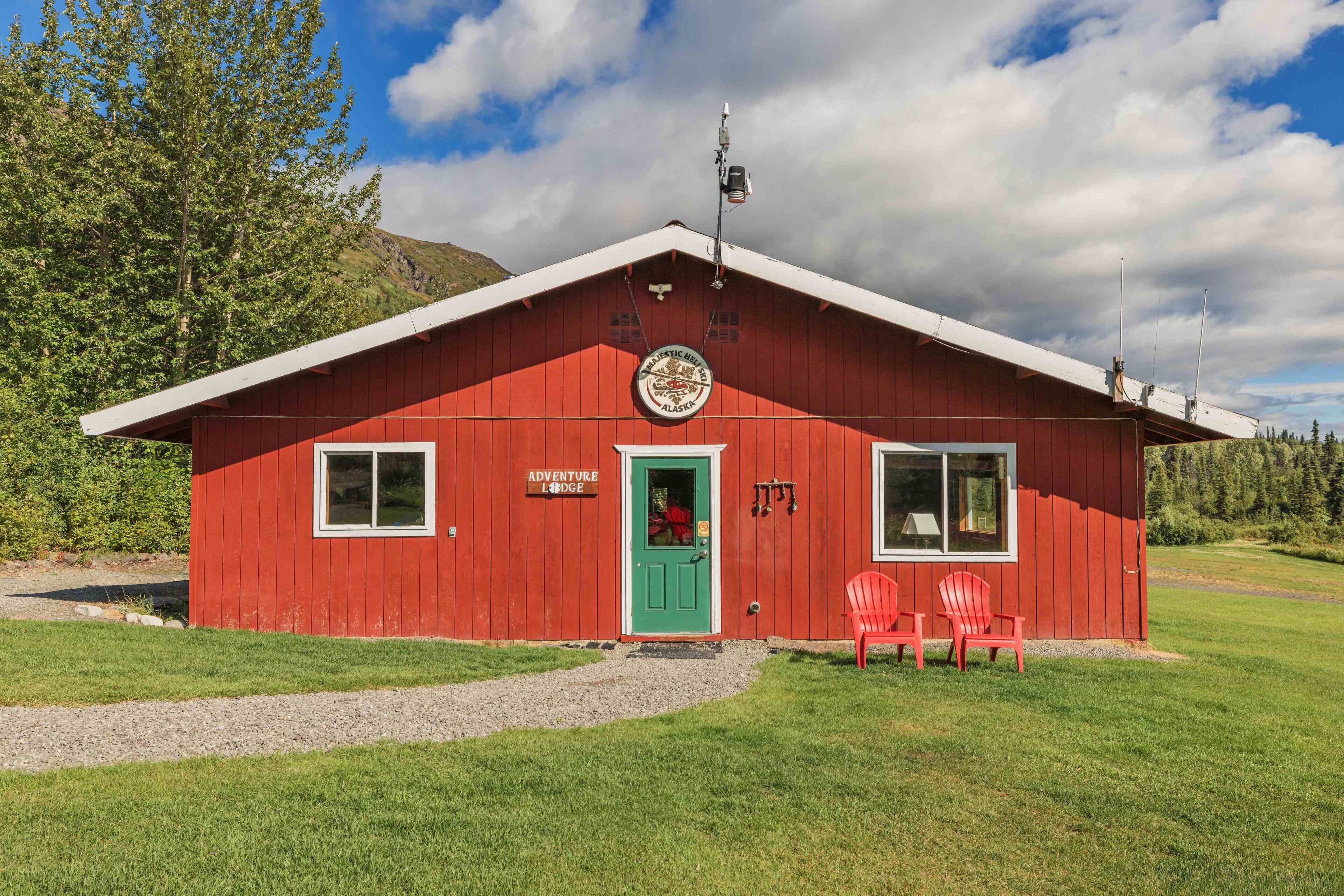 Un edificio rojo con puerta verde, dos ventanas y un letrero que dice 'Adventure Lodge'.