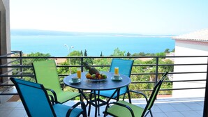 Ein Balkon mit Tisch für zwei Personen, mit Obstschale und zwei Gläsern Orangensaft. Der Balkon bietet einen malerischen Blick auf das Meer und das entfernte Land.