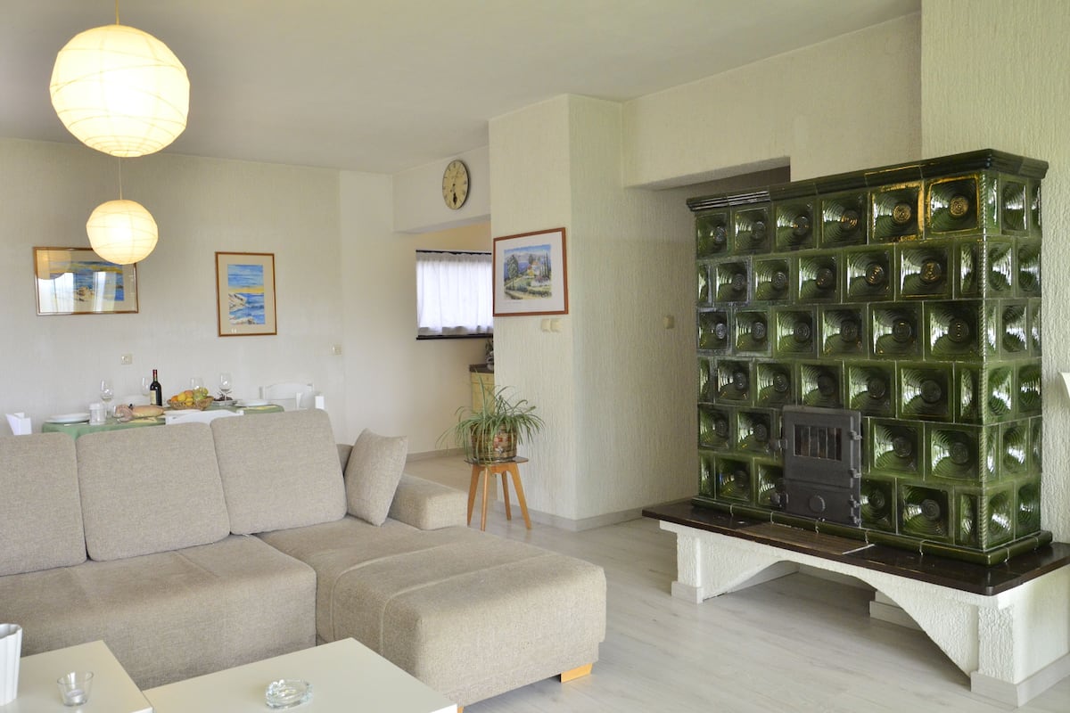 Una sala de estar moderna con un sofá modular, una chimenea con bloques de vidrio verde y un comedor con una mesa dispuesta para dos.