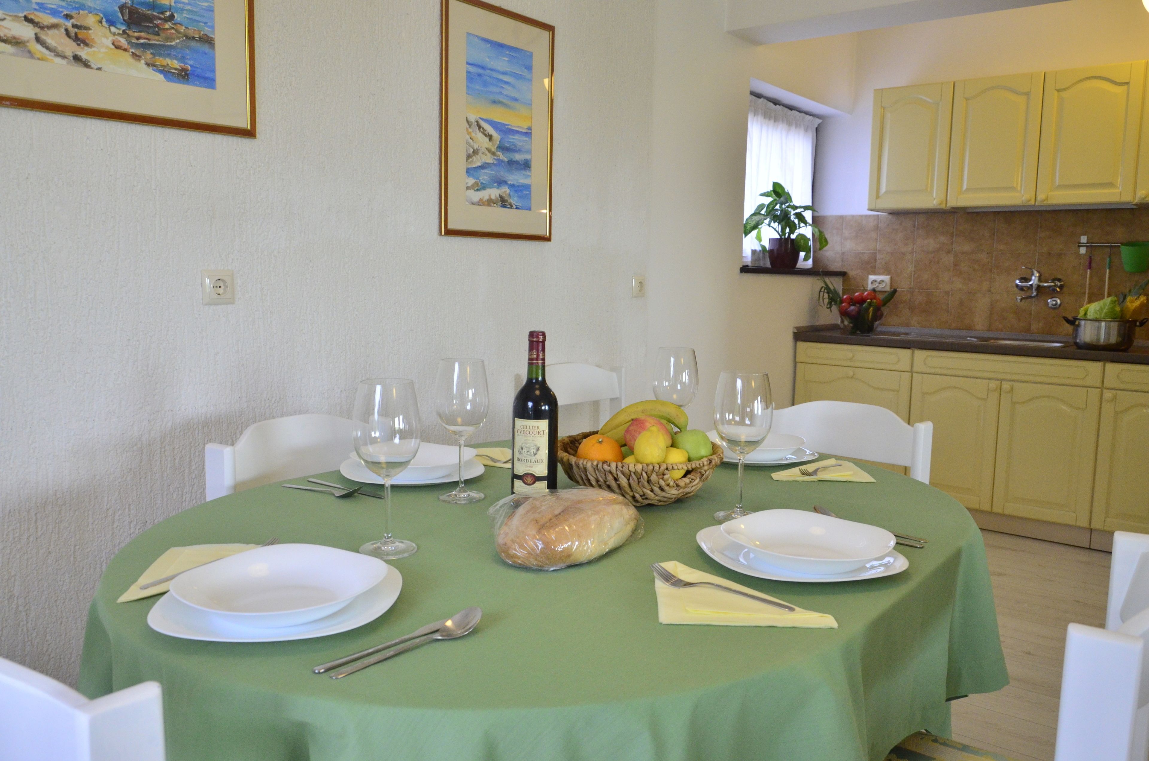A dining table set for four with plates, wine glasses, and a basket of fruit.