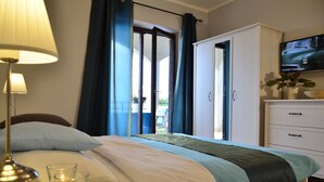 Ein Hotelzimmer mit einem Bett, einer Nachttischlampe, einem an der Wand befestigten Fernseher und Blick ins Freie durch eine Tür.