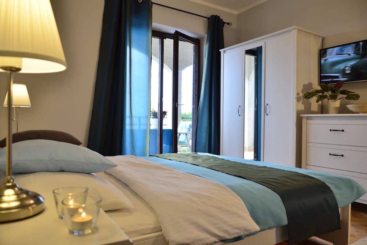 Habitación de hotel con una cama, una lámpara de noche, un televisor montado en la pared y vistas al exterior a través de una puerta.