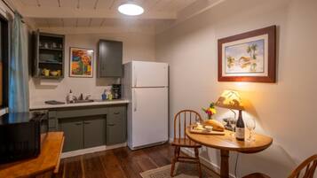 A compact kitchen with a refrigerator, a dining table with chairs, a coffee machine, and a painting on the wall.
