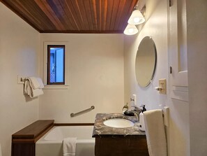 A bathroom with a bathtub, a sink with a marble countertop, a mirror, and a window with a view.