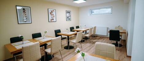 A conference room with multiple tables and chairs, framed artwork on the walls, and a window providing natural light.