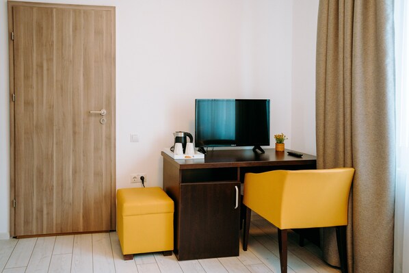 A room with a wooden door, a desk with a computer, a yellow chair, and a small stool.