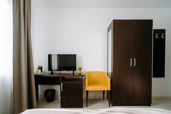 A hotel room with a bed, a desk with a television, a yellow chair, and a wardrobe.